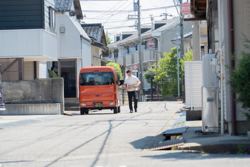 住宅街でオレンジ色の配送車から荷物を運ぶ配送スタッフ